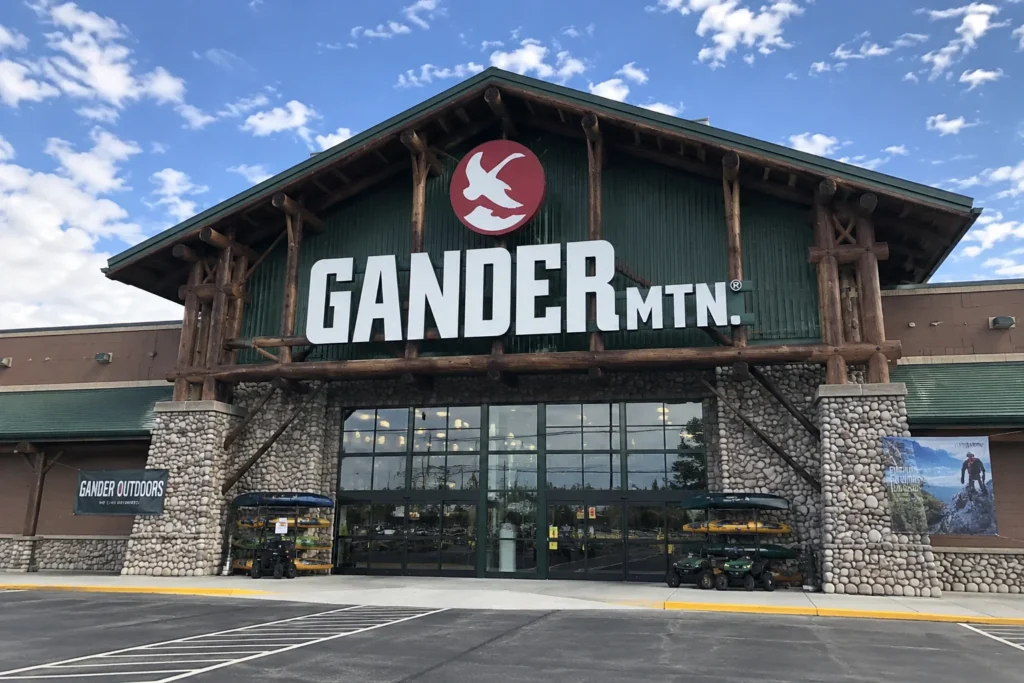 Front view of a Gander Mountain outdoor retail store featuring a large rustic building with timber beams, stone accents, and outdoor gear displays near the entrance.